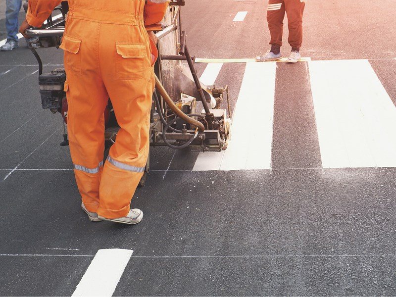 Road workers painting pedestrian crossing lines on a road. 