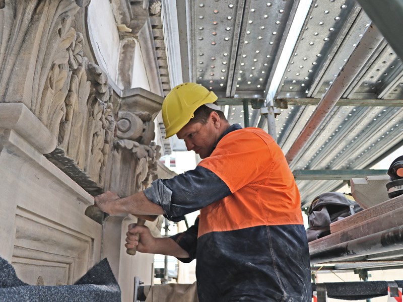 Glenn Torbet, stonemason, stands amongst scaffolding as he works on the stonework of Parliament House.