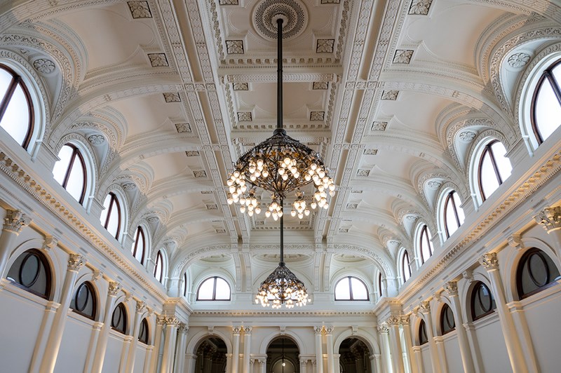 A ceiling of a white hall with arches and two large chandeliers.