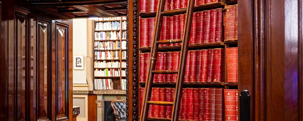 A ladder leaning over a shelf full of red leather-bound books in a library