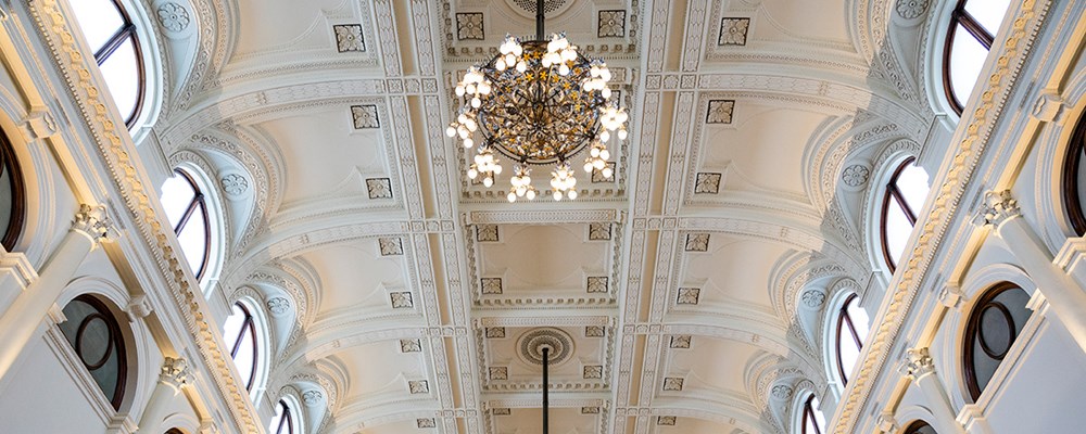 A large room with high ornate ceilings, arches and two chandeliers.