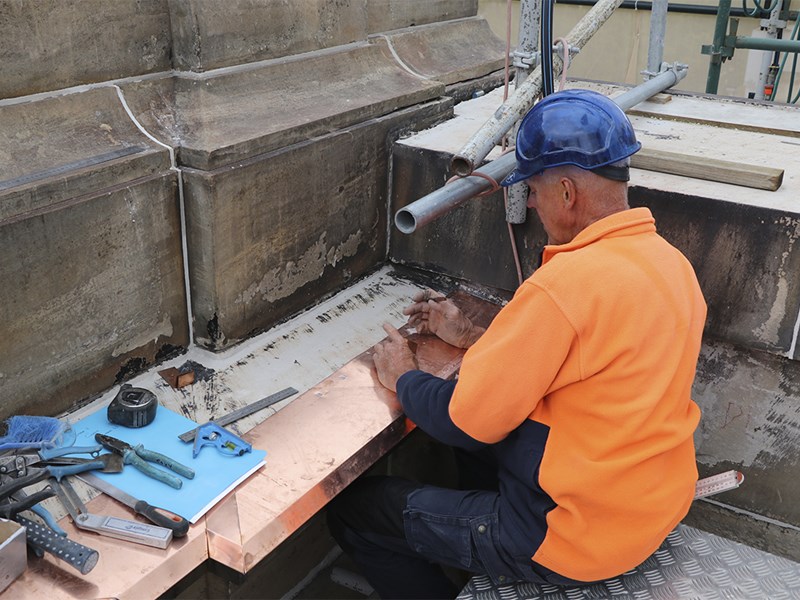 Chris Cox, stonemason, works on the drainage of Parliament House's roof. He is surrounded by tools.