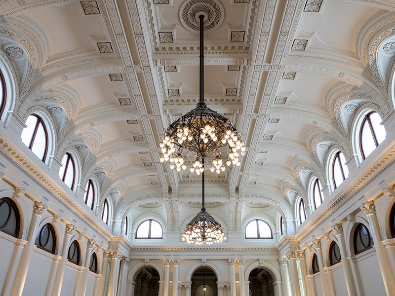 A ceiling of a white hall with arches and two large chandeliers.