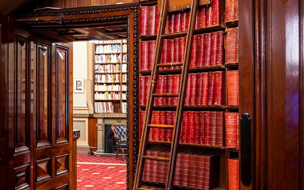 A ladder leaning over a shelf full of red leather-bound books in a library