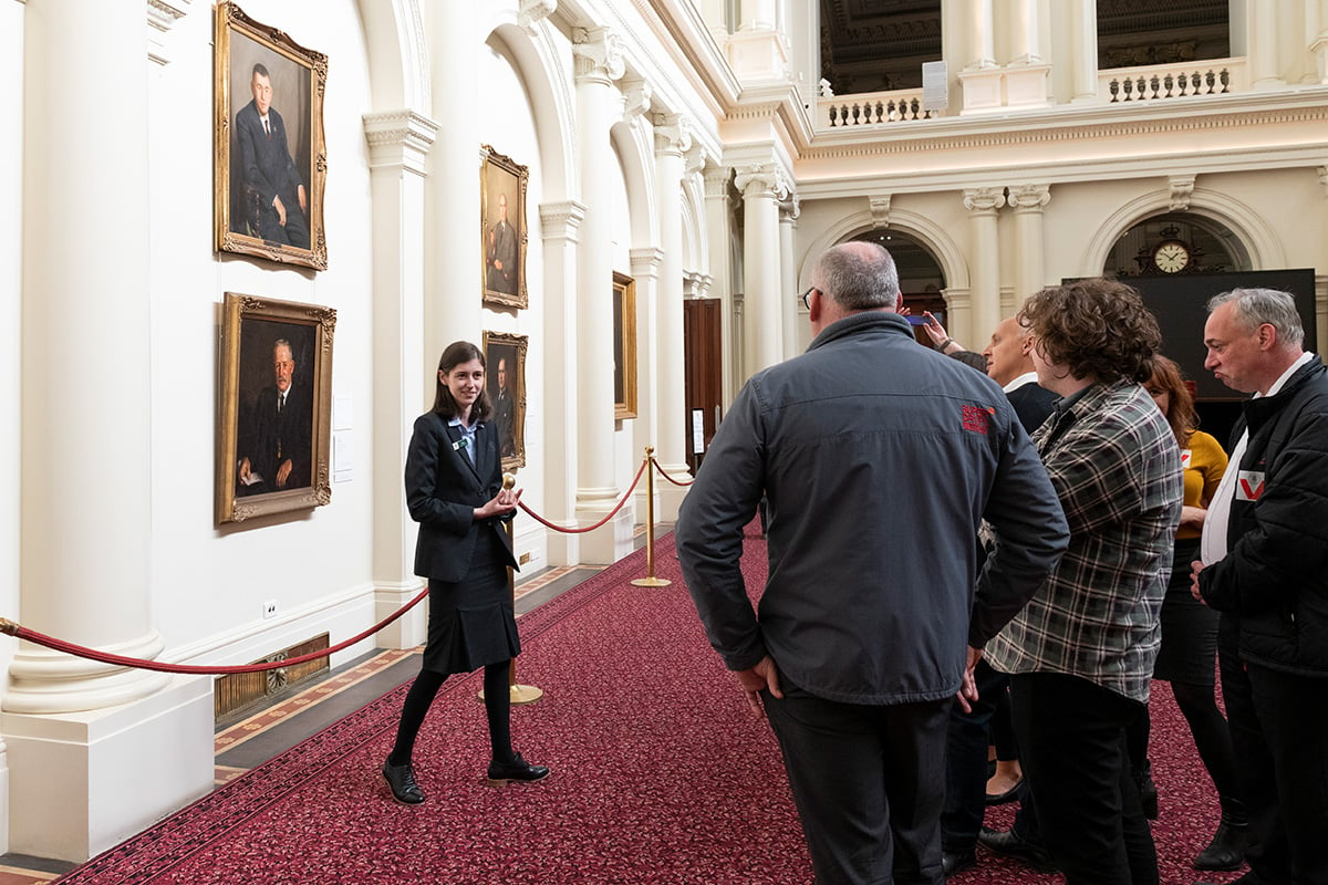 A tour of Queen's Hall, with the tour guide showing guests the Premiers' portrait collection.